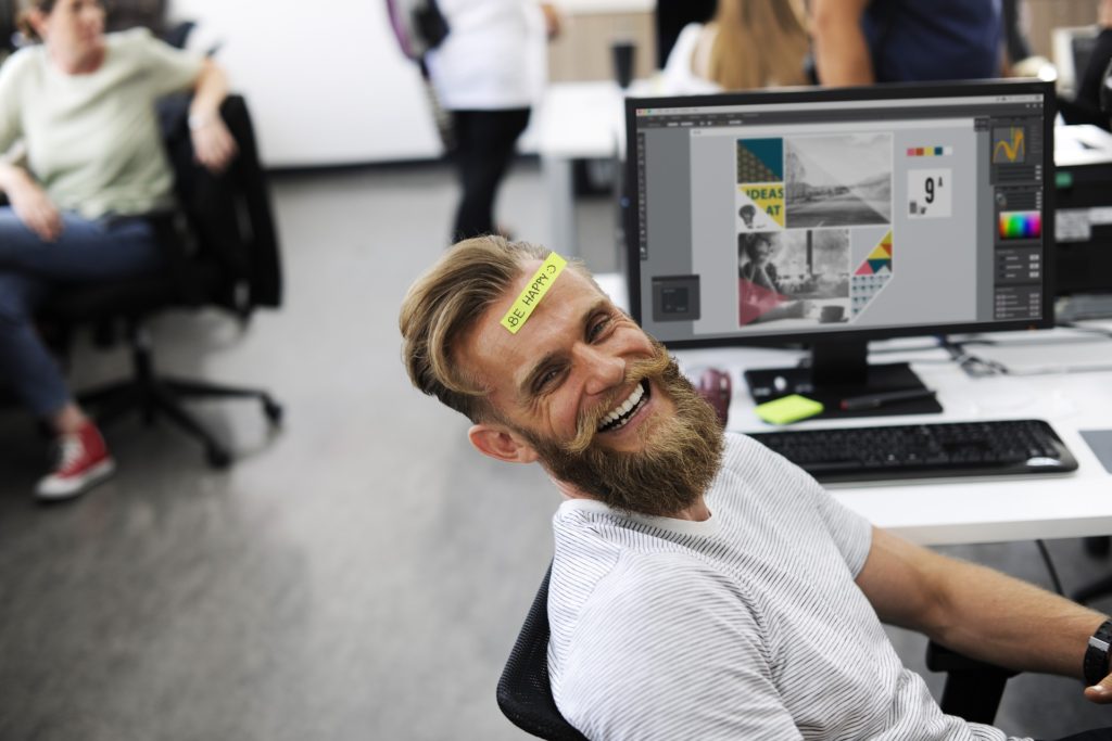 Homem sorrindo no trabalho com mensagem de felicidade pregada na testa