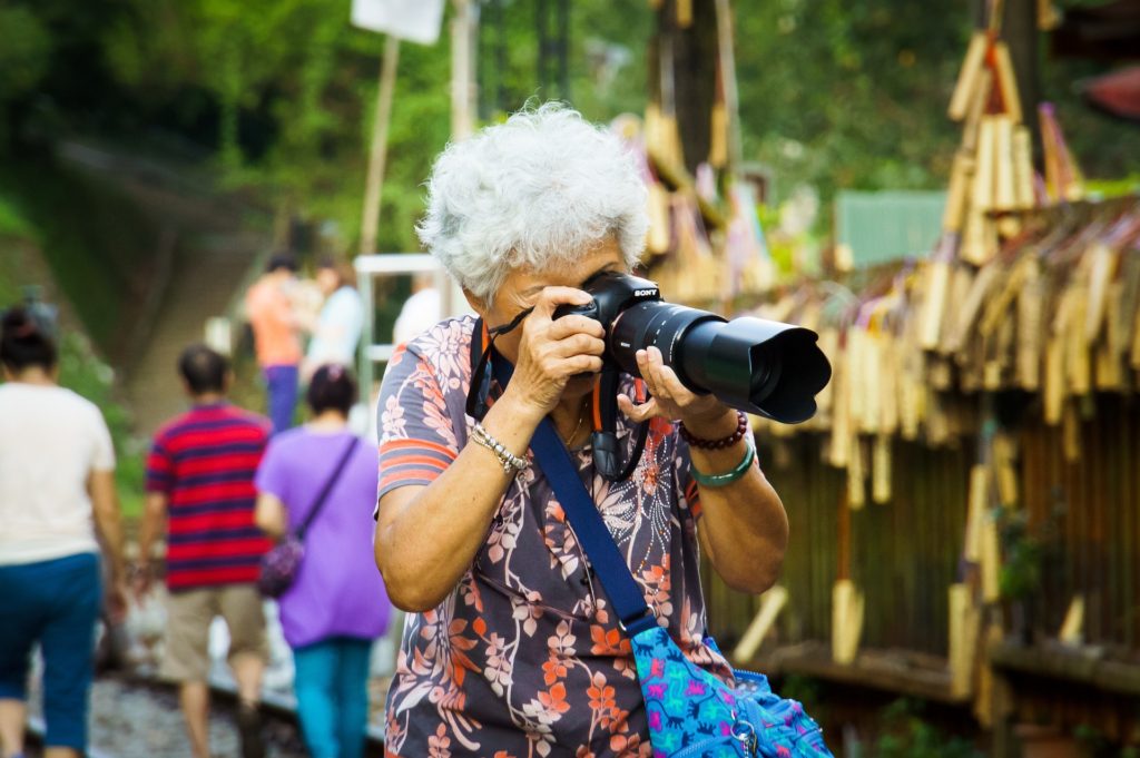 Senhora asiática, cabelos brancos, empunhando uma máquina fotográfica com uma teleobjetiva