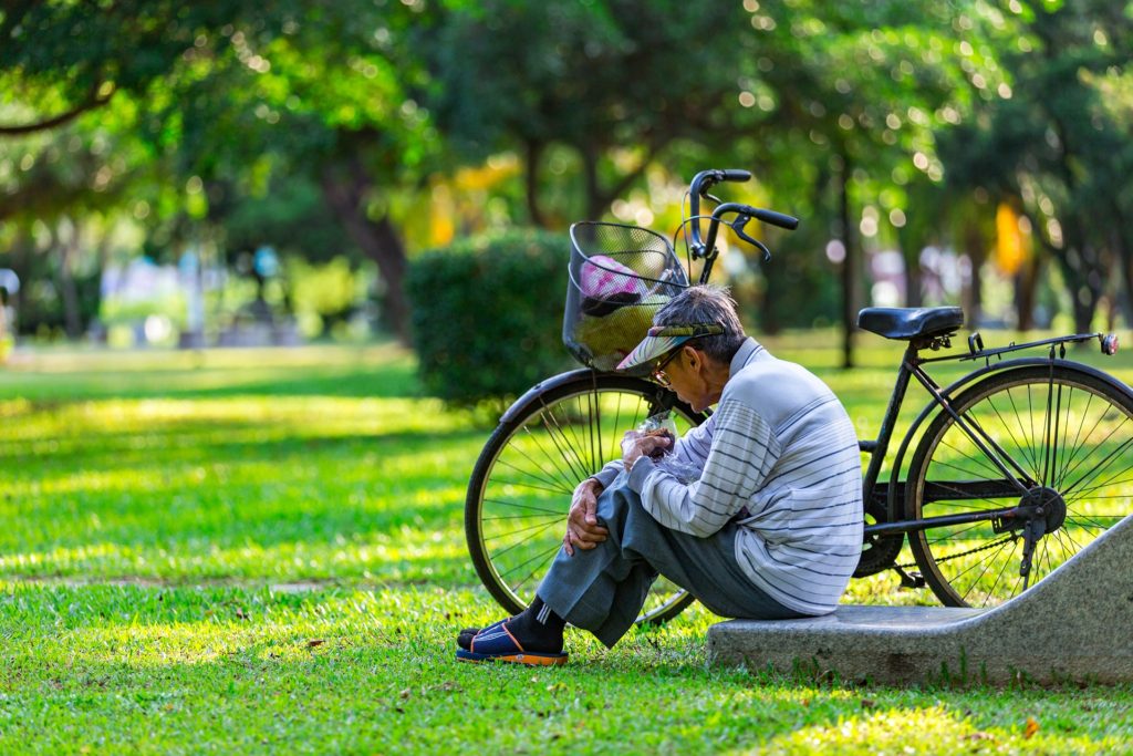 Senhor japonês de boné sentado ao lado da sua bicicleta em um parque 