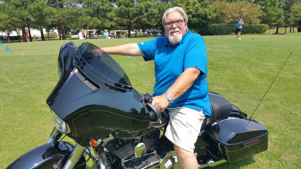 Homem branco, de cabelo e barba branca, sentado em uma moto super potente