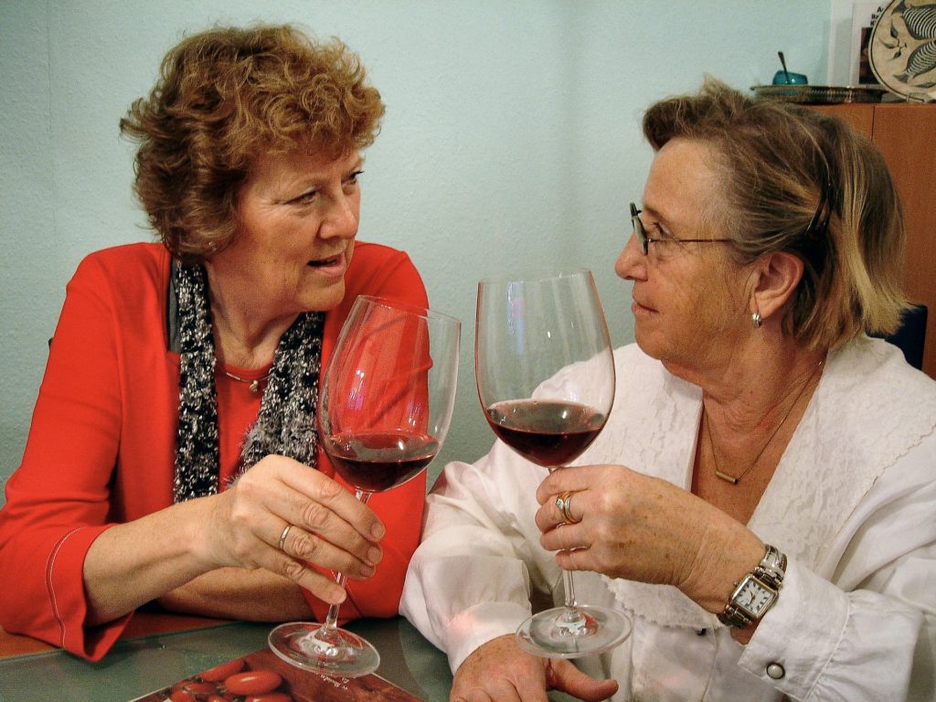 Mulheres brancas, idosas, brindando com duas taças de vinho tinto